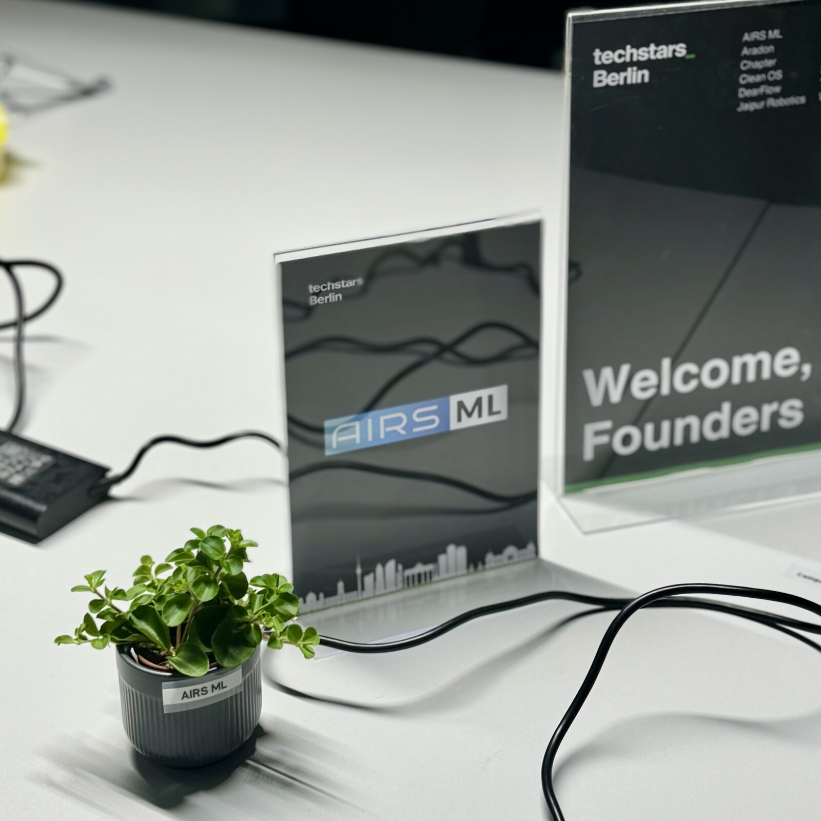 Welcome Founders signage with an AIRS ML startup table marker and labelled plant at Techstars Berlin